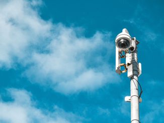 Camera giám sát dạng vòm màu trắng gắn trên cột kim loại cùng các thiết bị truyền tín hiệu, nền trời xanh có mây.