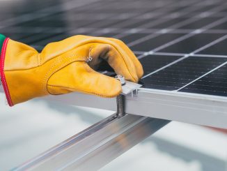 Bàn tay đeo găng bảo hộ siết kẹp giữ tấm pin mặt trời trên thanh ray nhôm