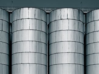Cận cảnh bốn silo thép hình trụ đứng sát nhau, trên đỉnh có lối đi và lan can, nền trời xanh sẫm