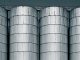 Cận cảnh bốn silo thép hình trụ đứng sát nhau, trên đỉnh có lối đi và lan can, nền trời xanh sẫm