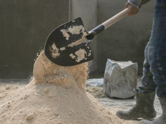 Người lao động dùng xẻng xúc cát trên công trường, bên cạnh là một bao vật liệu
