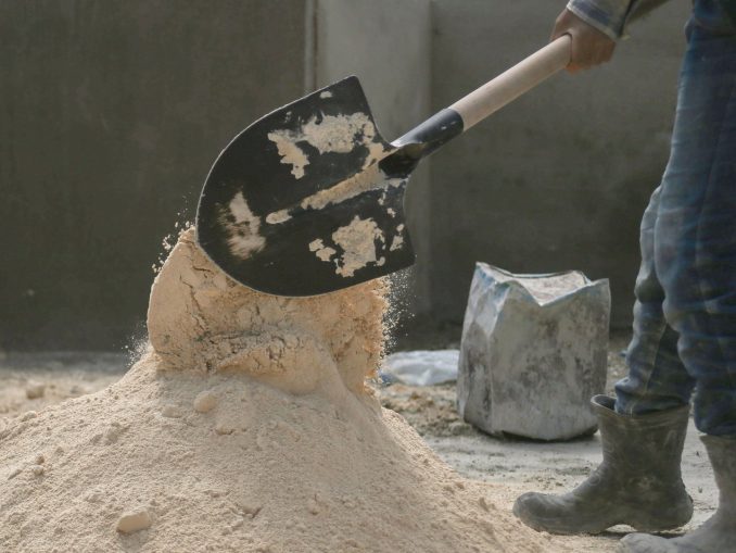 Người lao động dùng xẻng xúc cát trên công trường, bên cạnh là một bao vật liệu